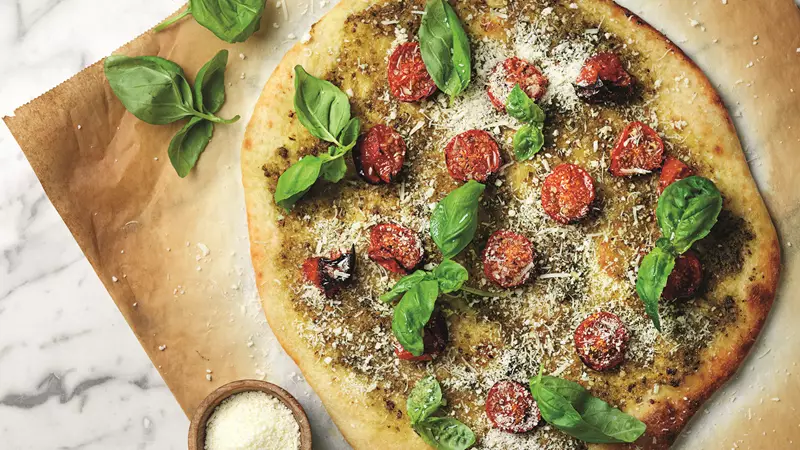 Nybakad pizza med pesto och tomater bakad på färsk pizzadeg